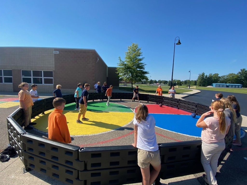 Students playing on the playground a new game called Gaga Ball.  It is played inside an octagonal pit.