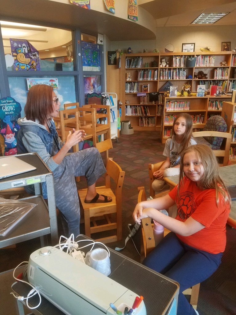 Mrs. Price is in the library with two students showing them how to use the mug press.