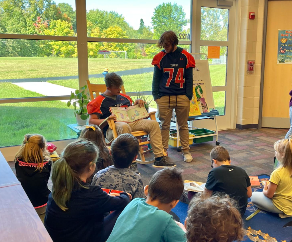 Football players reading aloud to second graders. 