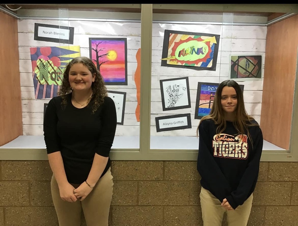 Alayna and Norah stand in front of their artwork display.